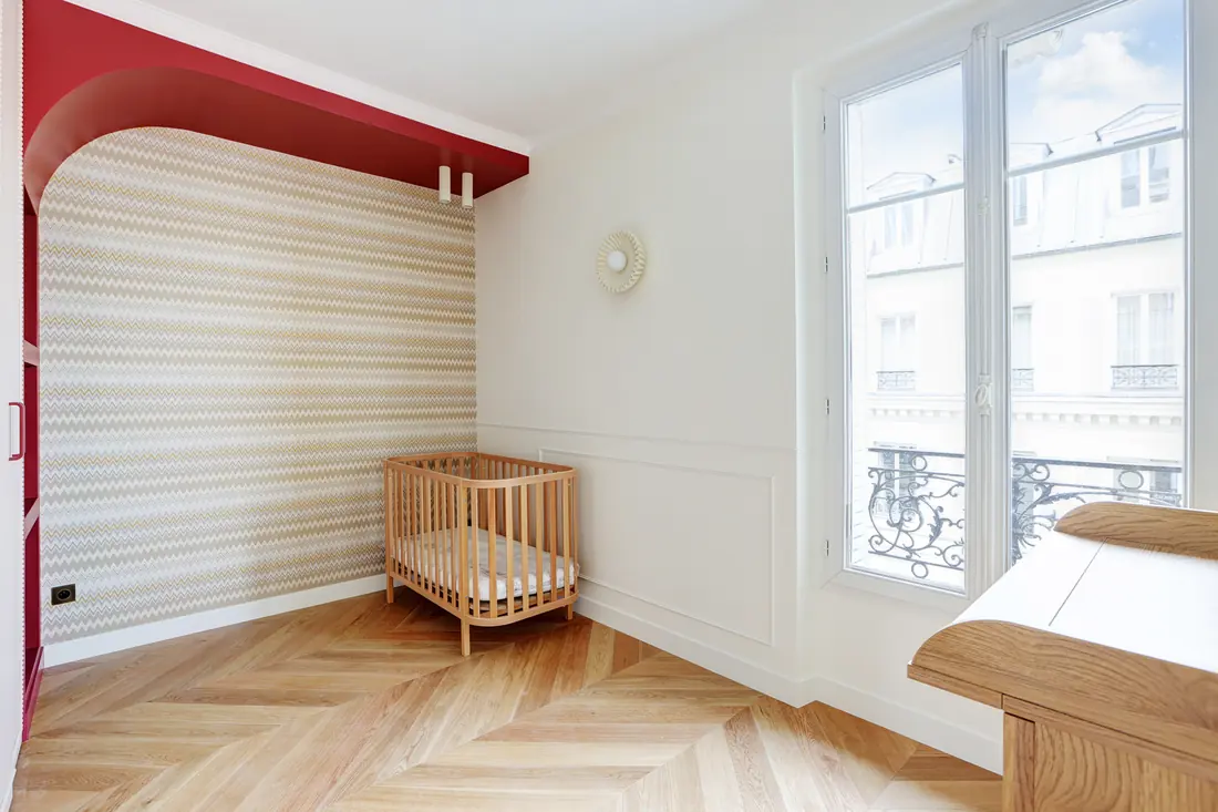 Chambre d'enfant avec lit à barreaux, table à langer et fenêtre sur les toits de Paris