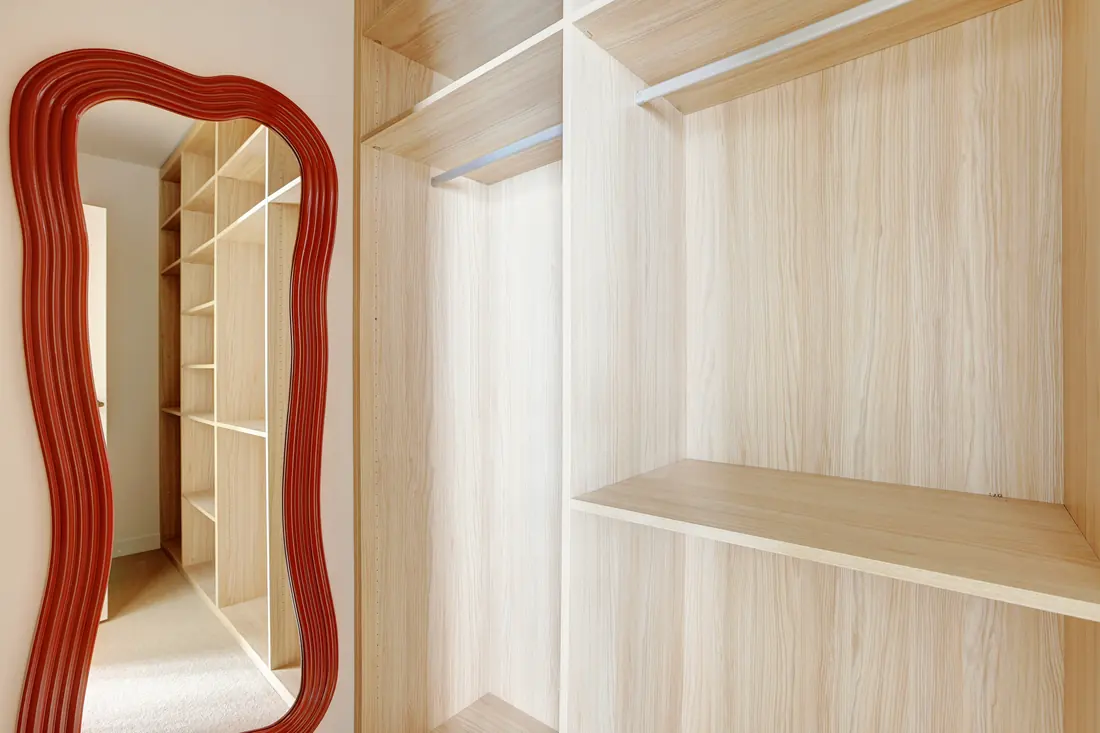 Dressing ouvert en bois clair avec penderies, étagères et grand miroir ondulé